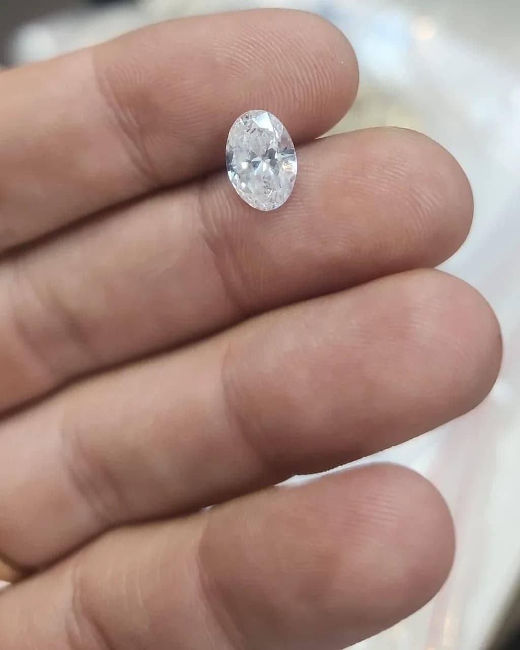 A loose oval brilliant diamond held between the maker's fingers