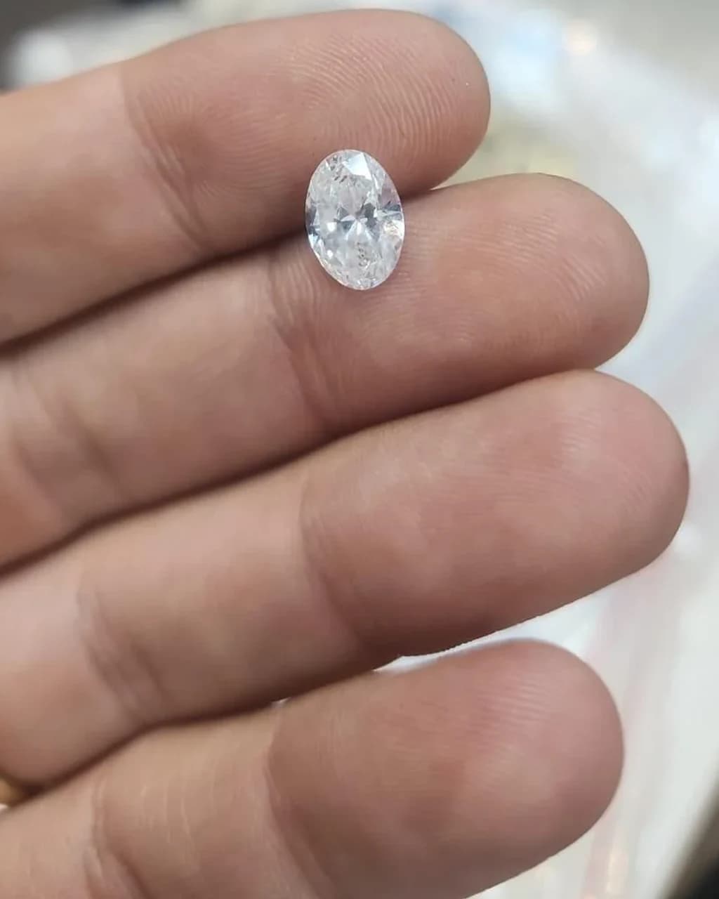 A loose oval brilliant diamond held between the maker's fingers
