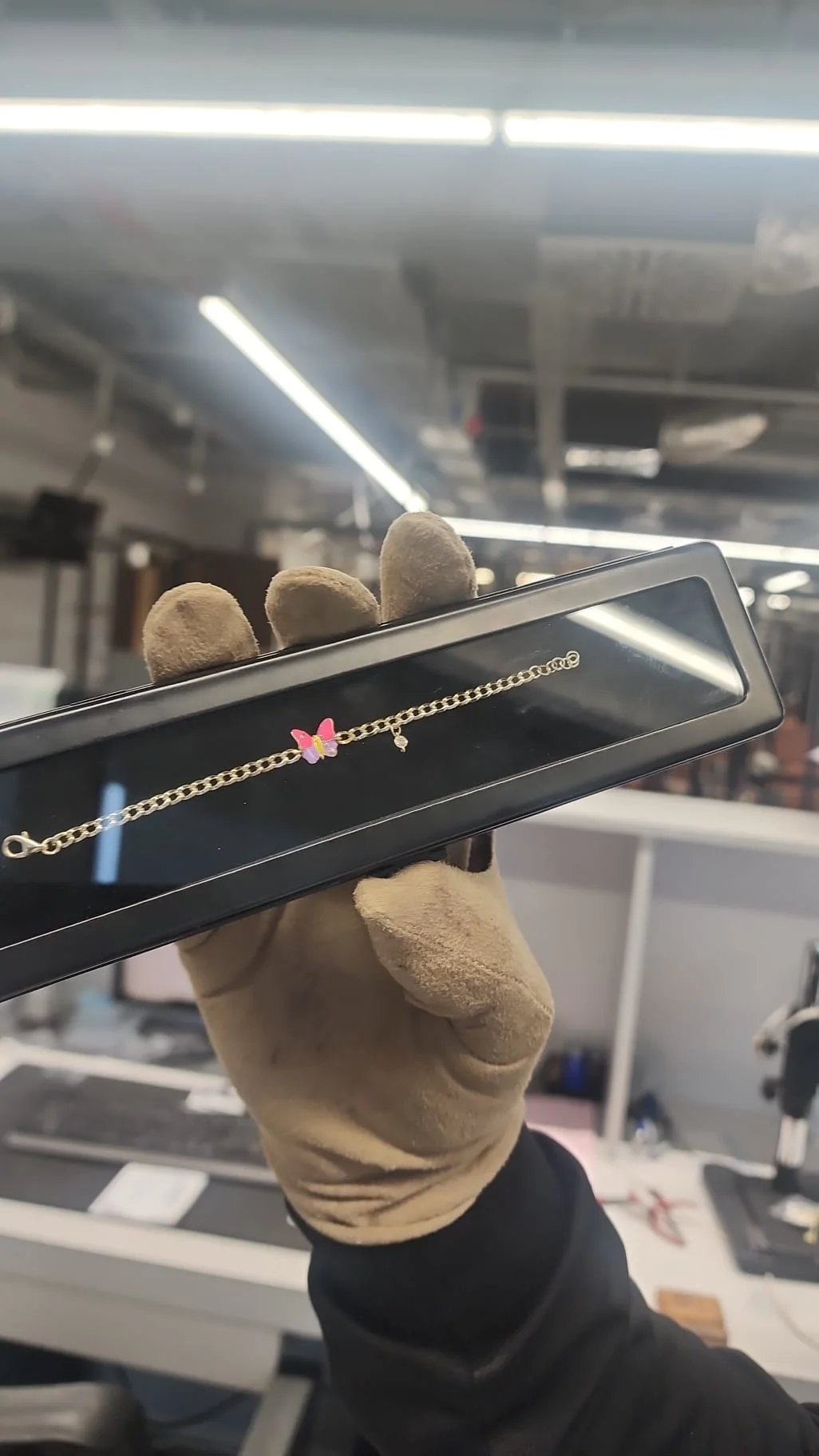 A finished gold bracelet held in a gloved hand at the atelier bench